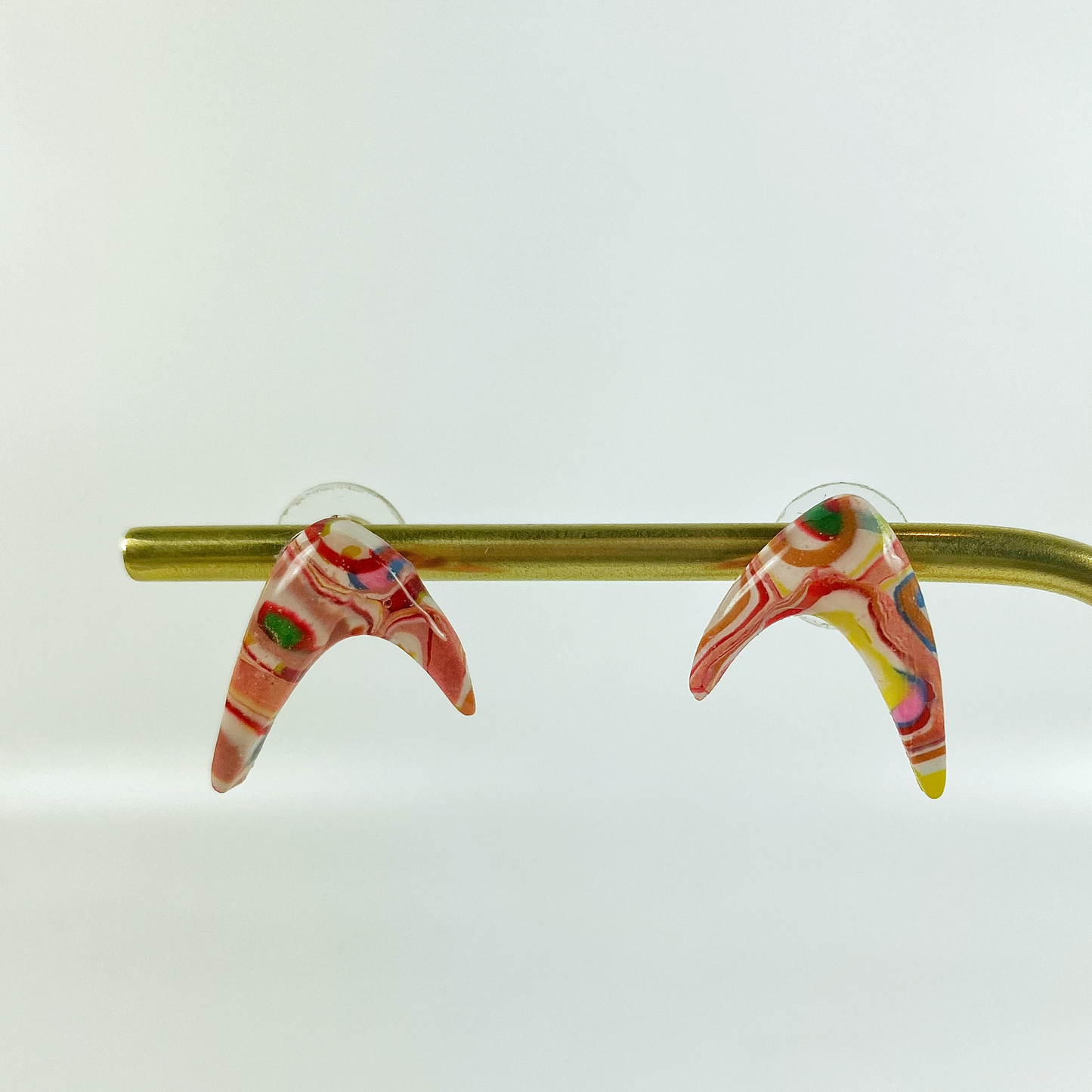 Pink Boomerang Stud Earrings on a brass earrings stand