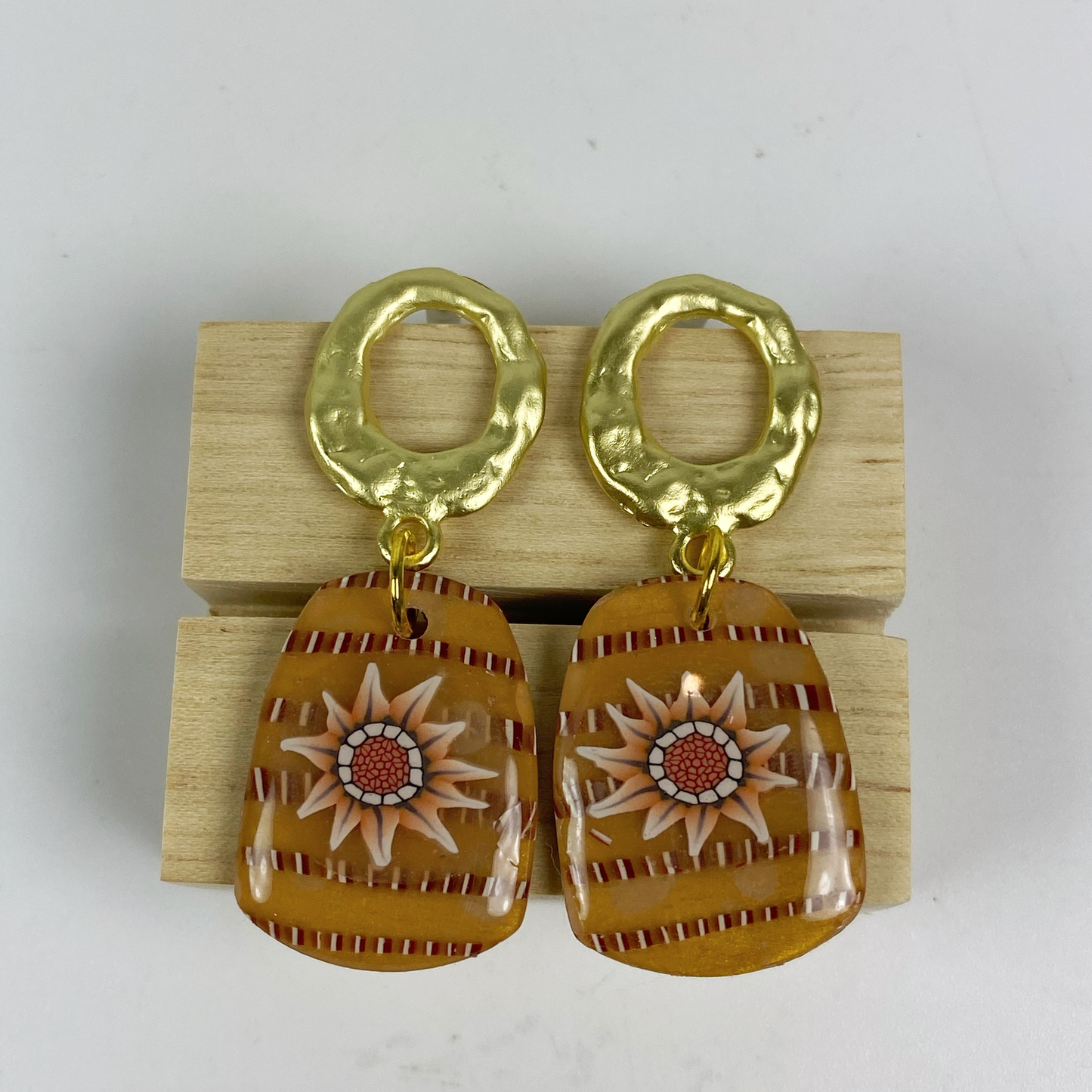 Saffron Daisy Polymer Clay Earrings  on a wooden block.