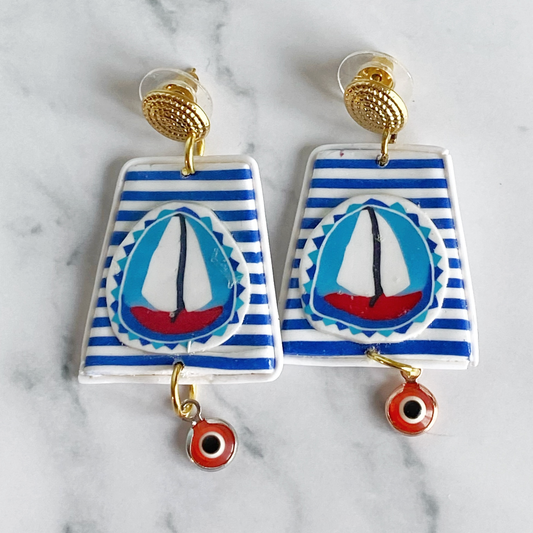 Handmade Polymer Clay Earrings with a blue and white striped background and a red sailboat with white sails on a marble background.