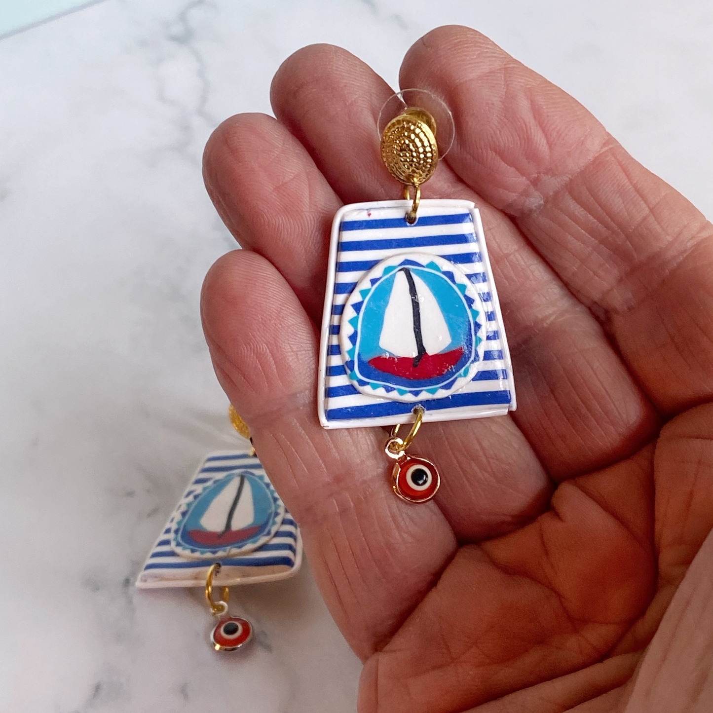 Handmade Polymer Clay Earrings with a blue and white striped background and a red sailboat with white sails handheld for size reference.