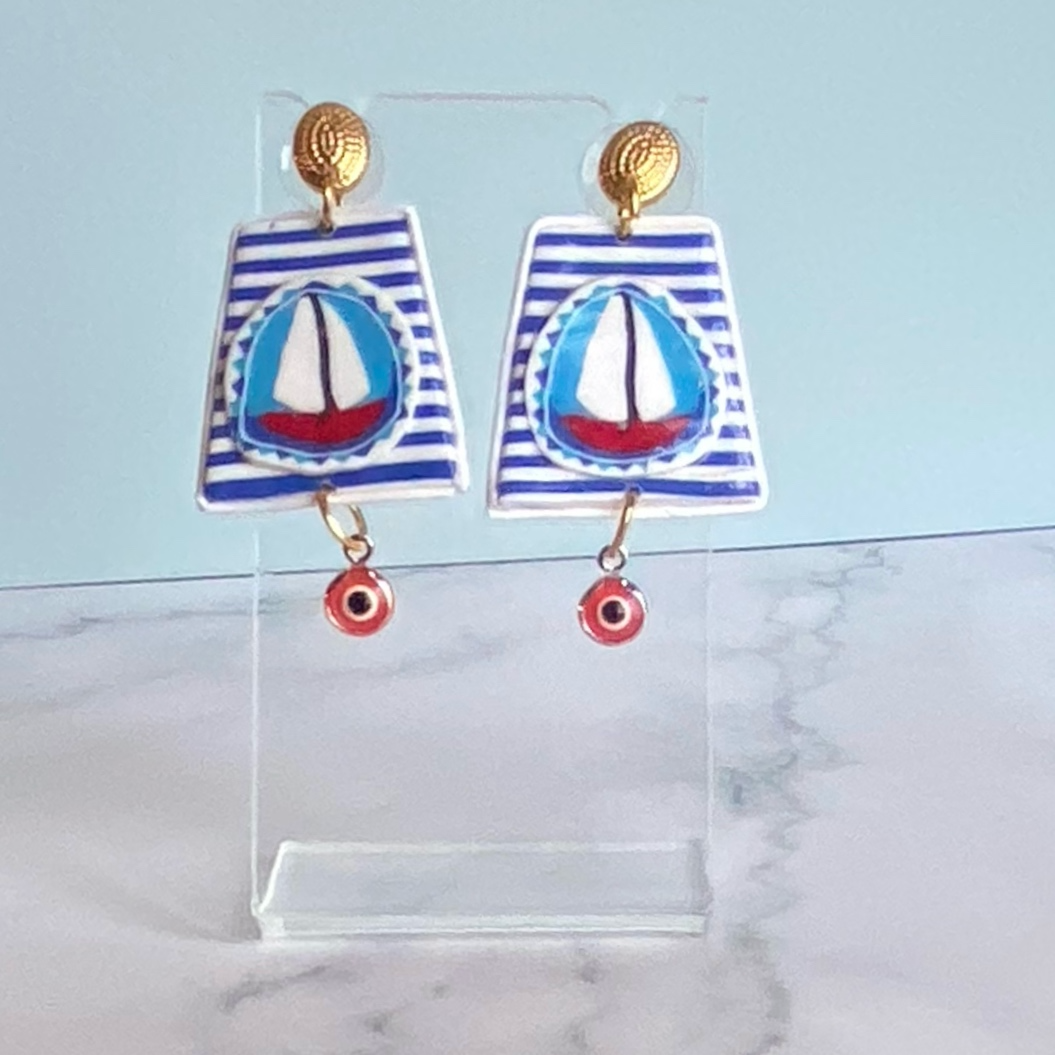 Handmade Polymer Clay Earrings with a blue and white striped background and a red sailboat with white sails on a clear acrylic stand.