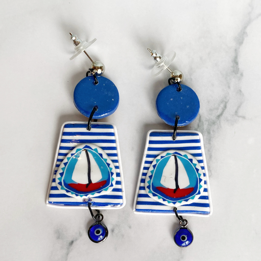 Blue and white striped handmade polymer clay sailboat earrings on a marble backtround.