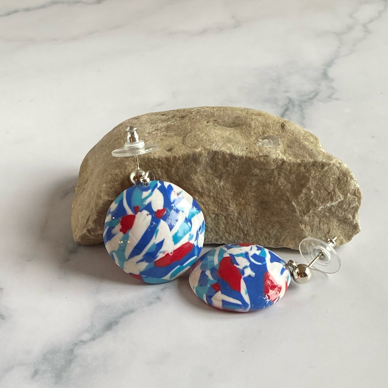 Handmade Polymer Clay Red White and Blue Earrings, posed against a rock