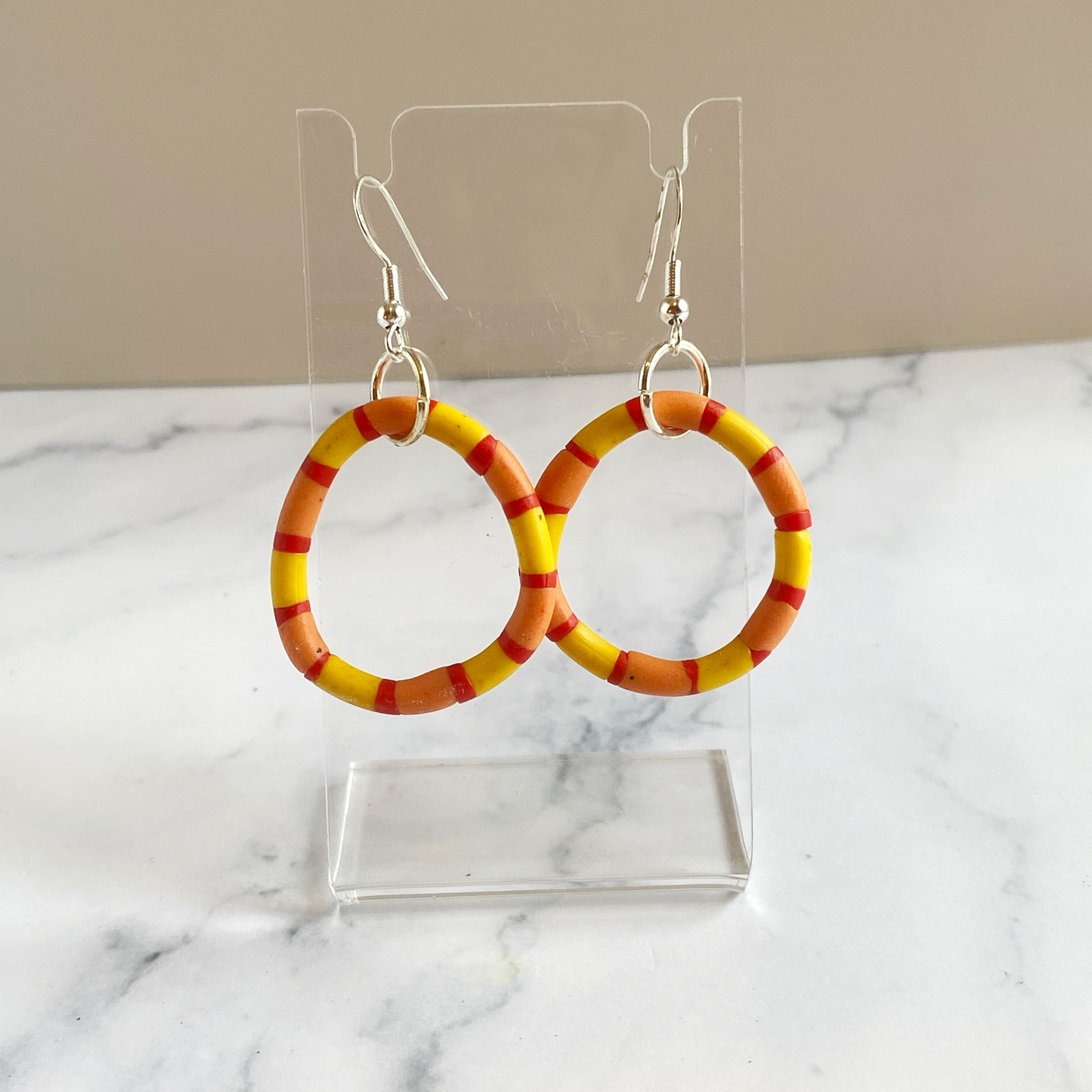 Handmade polymer clay rhythm hoops in red orange and yellow displayed on a clear acrylic stand