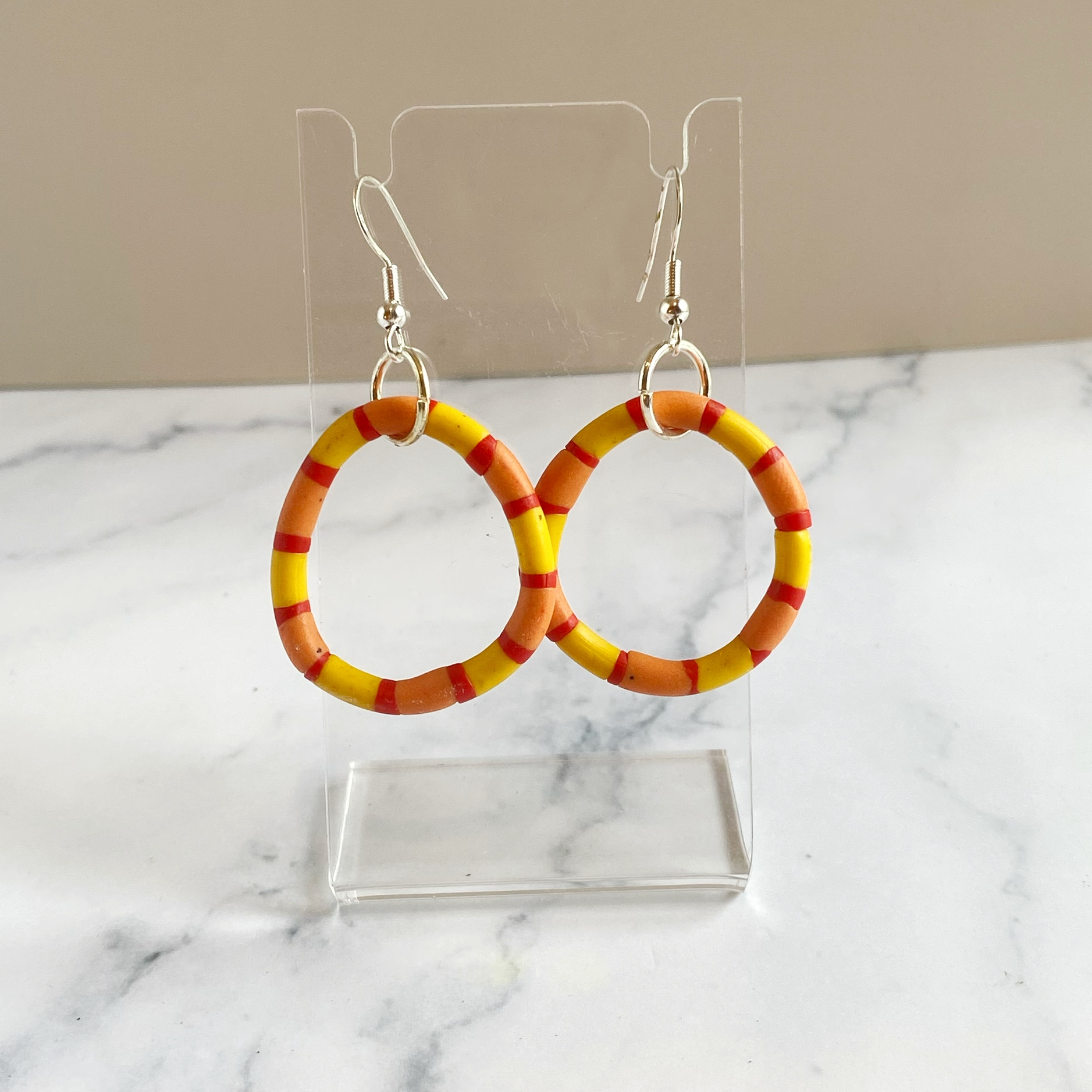 Handmade polymer clay rhythm hoops in red orange and yellow displayed on a clear acrylic stand
