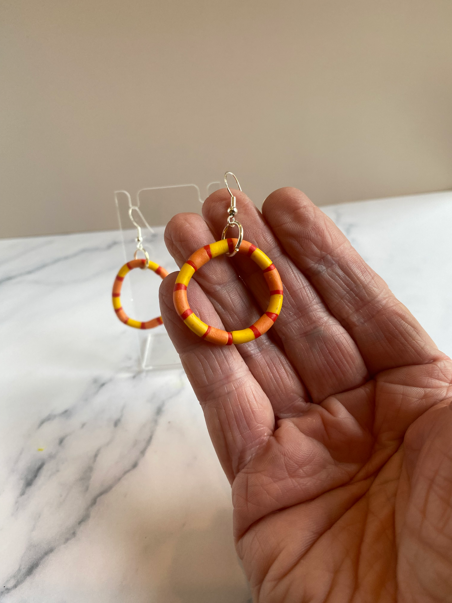 Handmade polymer clay rhythm hoops in red orange and yellow handheld for size reference. 