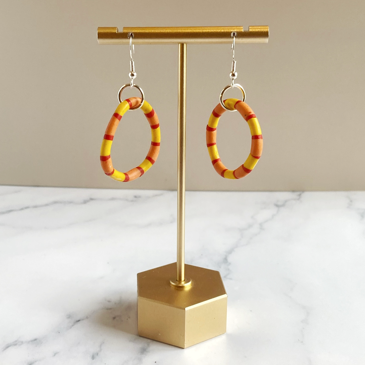 Handmade polymer clay rhythm hoops in red orange and yellow on a brass earring stand.  